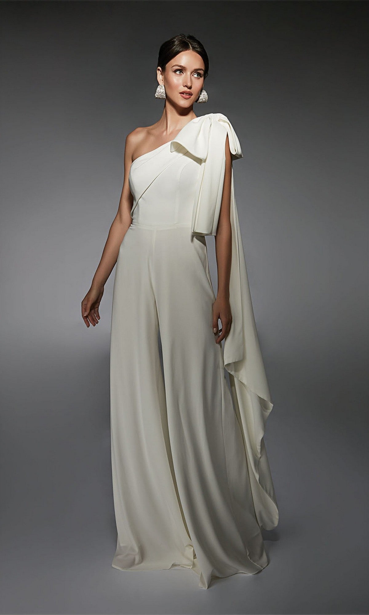 Woman in an ivory Alyce 70065 long formal jumpsuit with one shoulder, wide legs, and draped detail stands against a neutral gray background—a chic alternative to a cocktail dress.